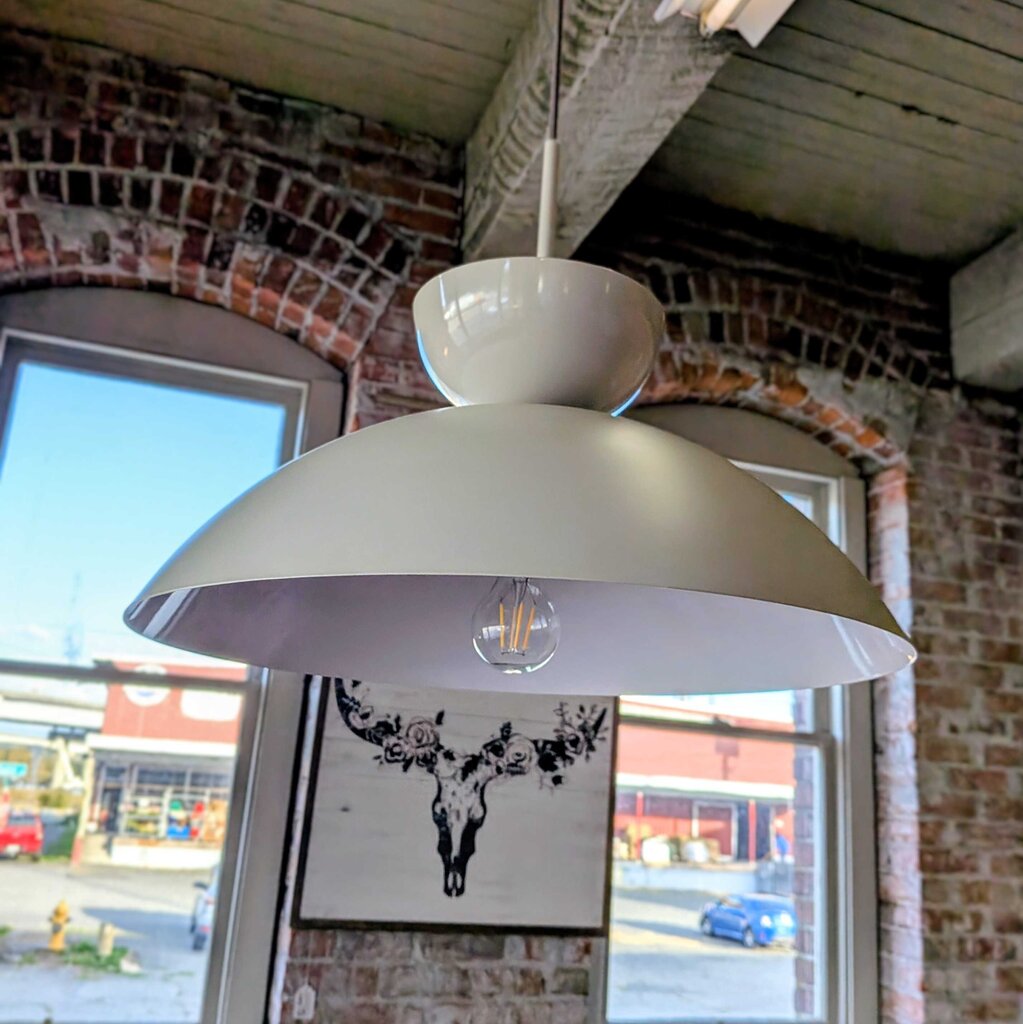 White pendant light hanging in a room with brick walls and large windows.