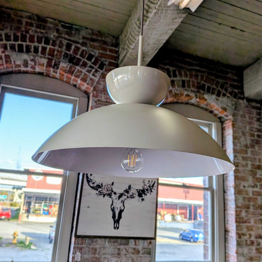 White pendant light hanging in a room with brick walls and large windows.