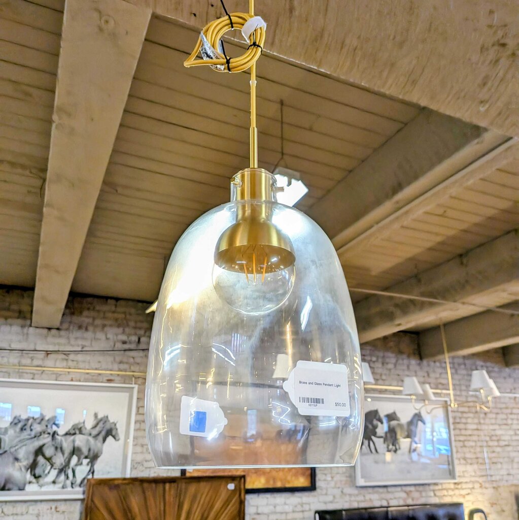 Clear glass pendant light with gold fixture hanging in a store setting.
