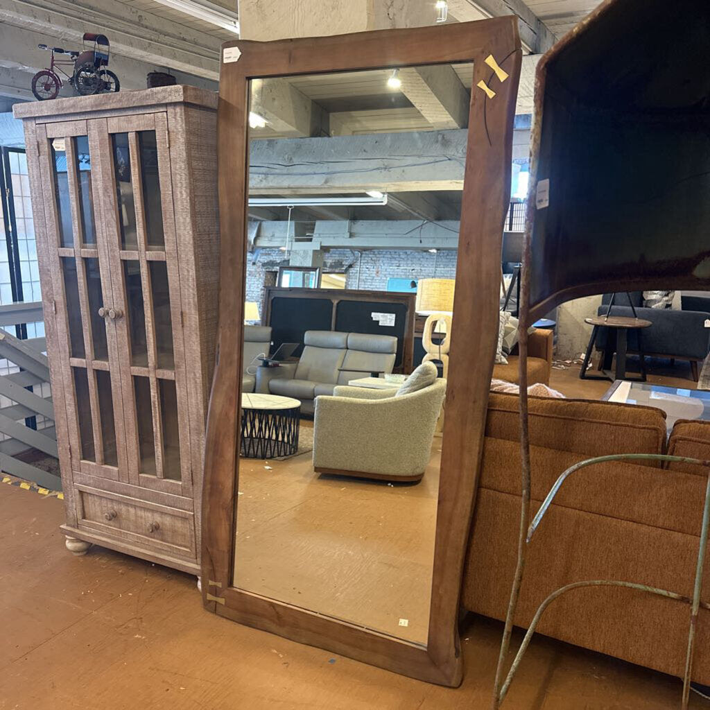 Large wooden-framed mirror in a furniture store setting with various items in the background.