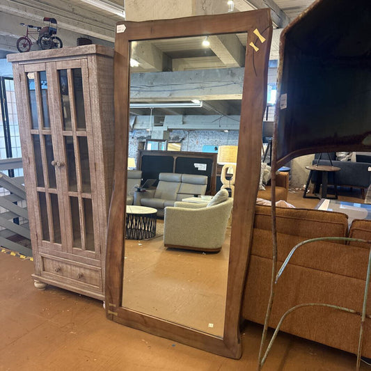 Large wooden-framed mirror in a furniture store setting with various items in the background.