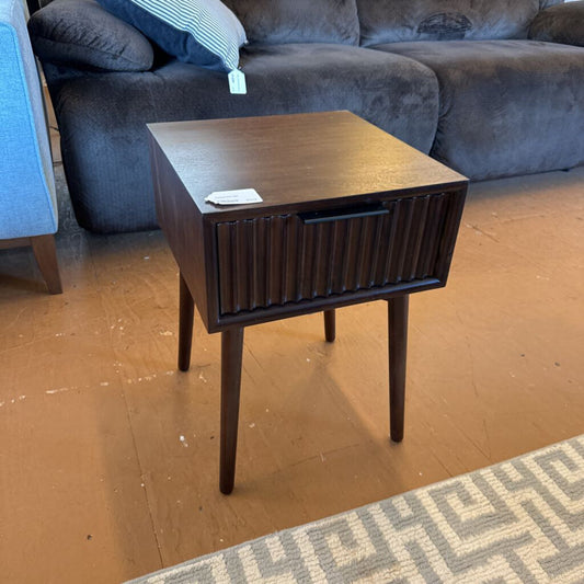 Wooden side table in a living room setting with a sofa and rug.