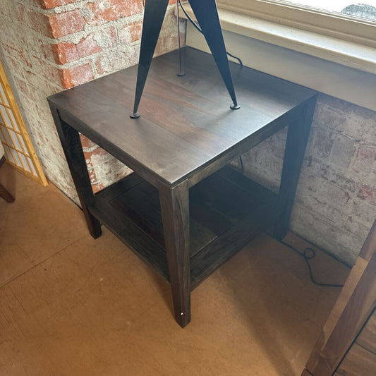 Small wooden table with metal legs against a brick wall.