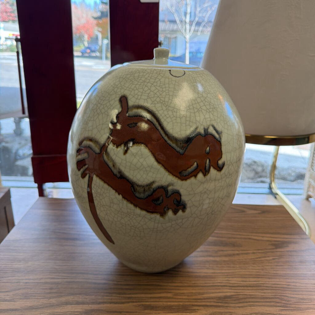 Decorative ceramic vase with a cracked glaze finish and brown abstract design on a wooden surface.