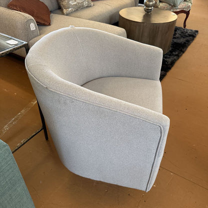 Gray curved armchair in a showroom setting with other furniture.