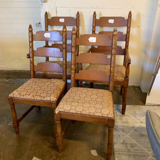 Set of wooden chairs with patterned seats in a room with a striped carpet and white walls.