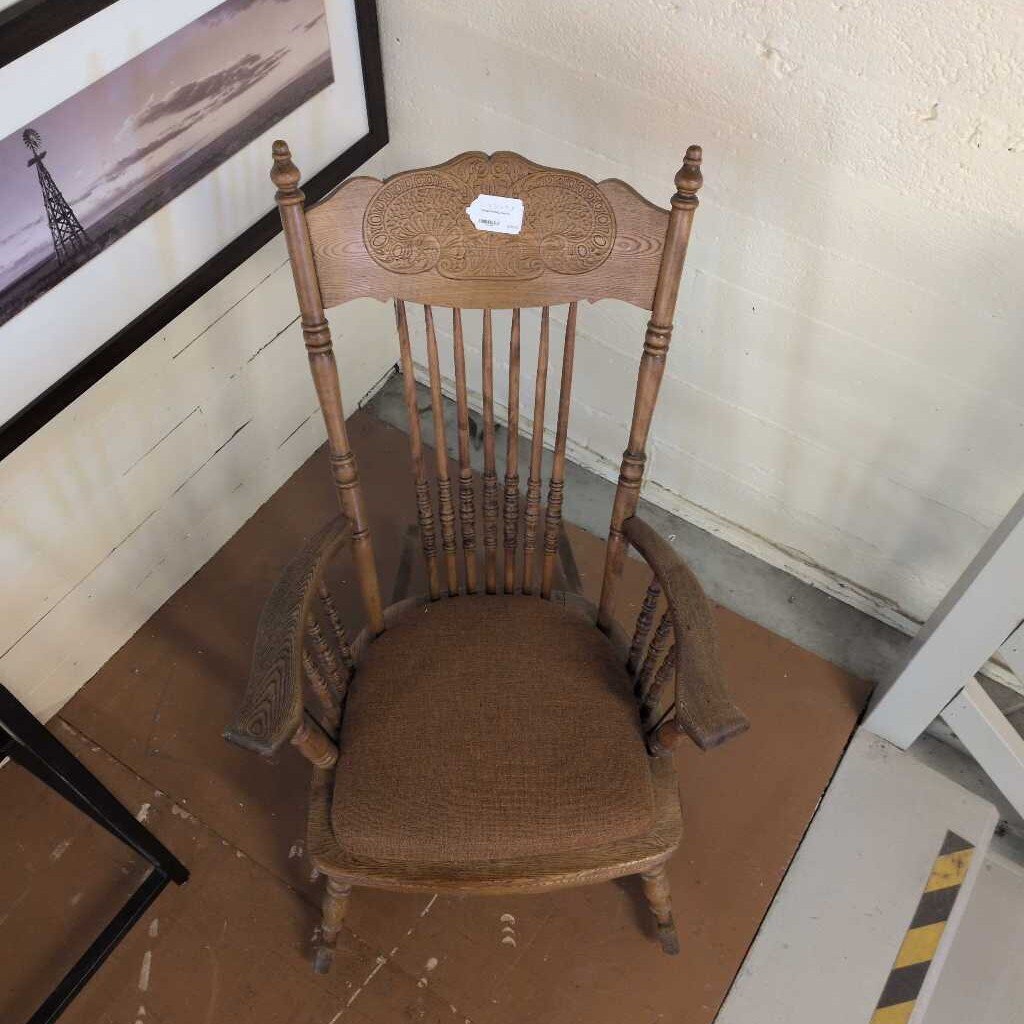 Wooden rocking chair with a worn cushion in a room with peeling paint.