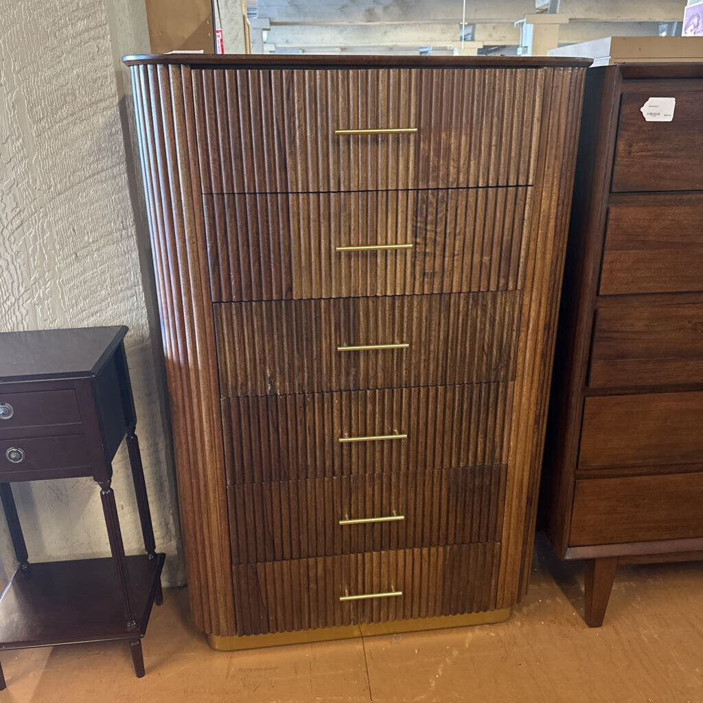 Wooden dresser with vertical slats and gold handles in a room setting.