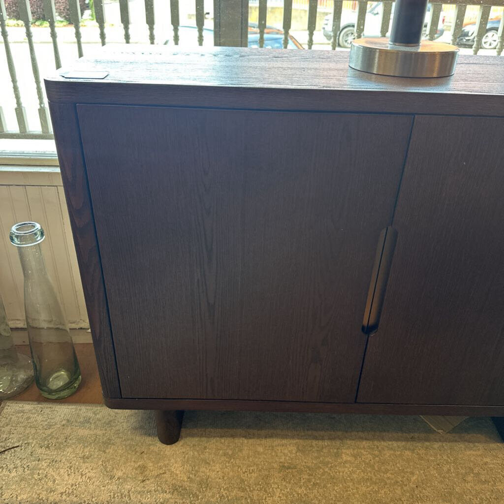 Dark wooden cabinet with a glass bottle on a windowsill in the background