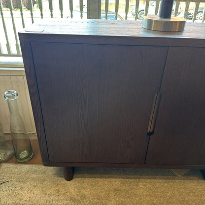 Dark wooden cabinet with a glass bottle on a windowsill in the background