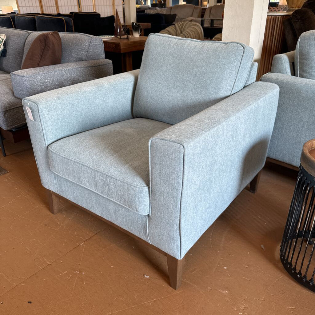 Gray armchair in a showroom setting with other furniture.