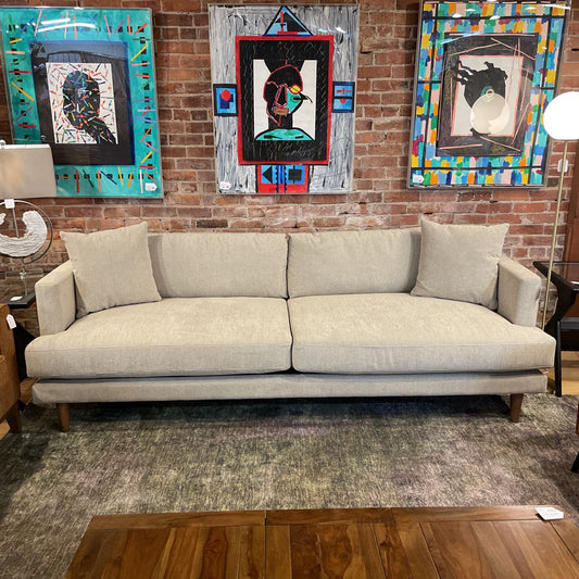 Gray sofa in a room with colorful abstract paintings on a brick wall.