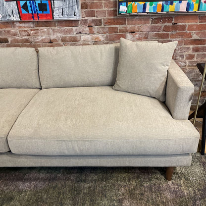 Beige sofa against a brick wall with colorful abstract art.