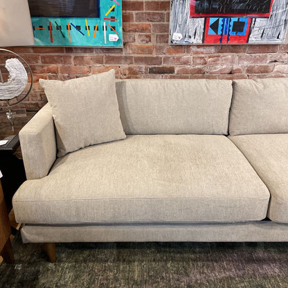 Beige sectional sofa in a room with abstract art on the wall.