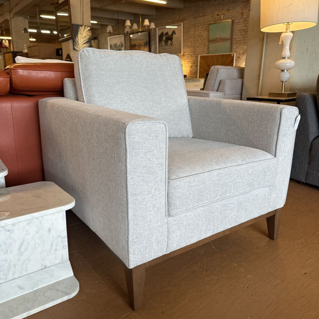 Gray armchair in a showroom setting with other furniture items.