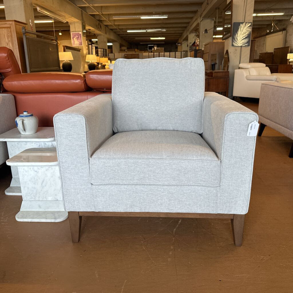 Gray armchair in a furniture store setting with other chairs and tables visible.