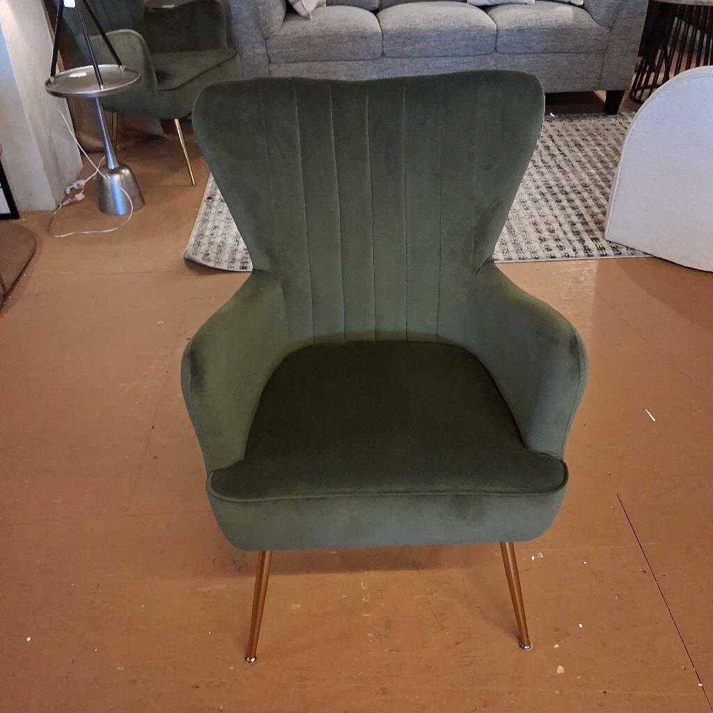 Green velvet chair with gold legs on a brown floor.