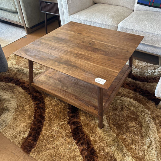 Wooden coffee table in a living room setting with a rug and sofa.