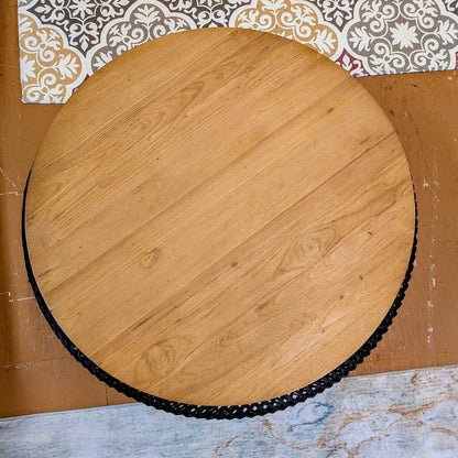 Round wooden cutting board with black rim on a patterned surface