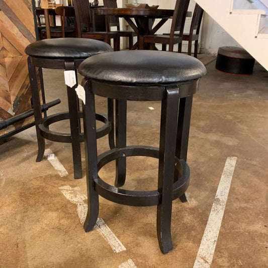 Two black bar stools with leather seats on a brown floor.