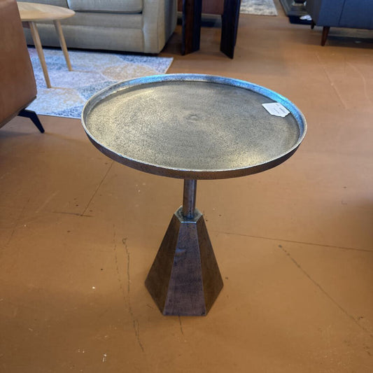 Metal side table with round top and cone-shaped base on a brown floor.