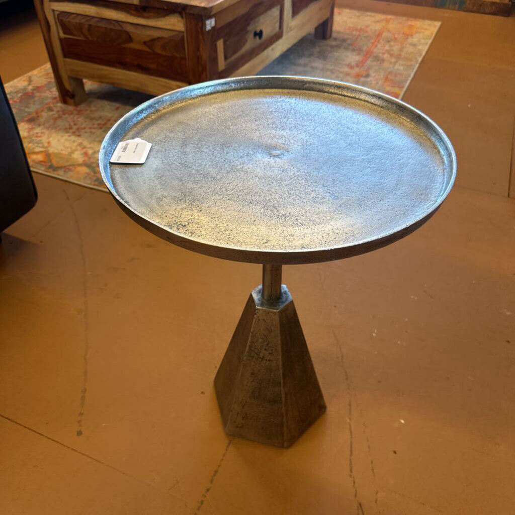 Small round metal table on a brown floor with a wooden cabinet in the background