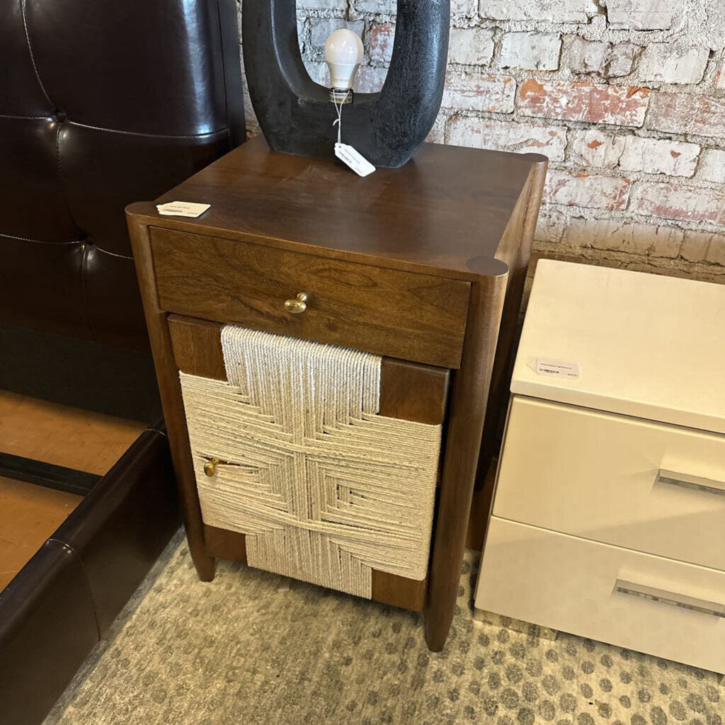 Wooden nightstand with woven design against a brick wall.