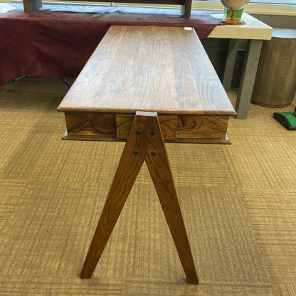 A slim, dark wood writing desk with a minimalist rectangular top, two open storage cubbies, and angled A-frame legs, shown on a neutral carpet.