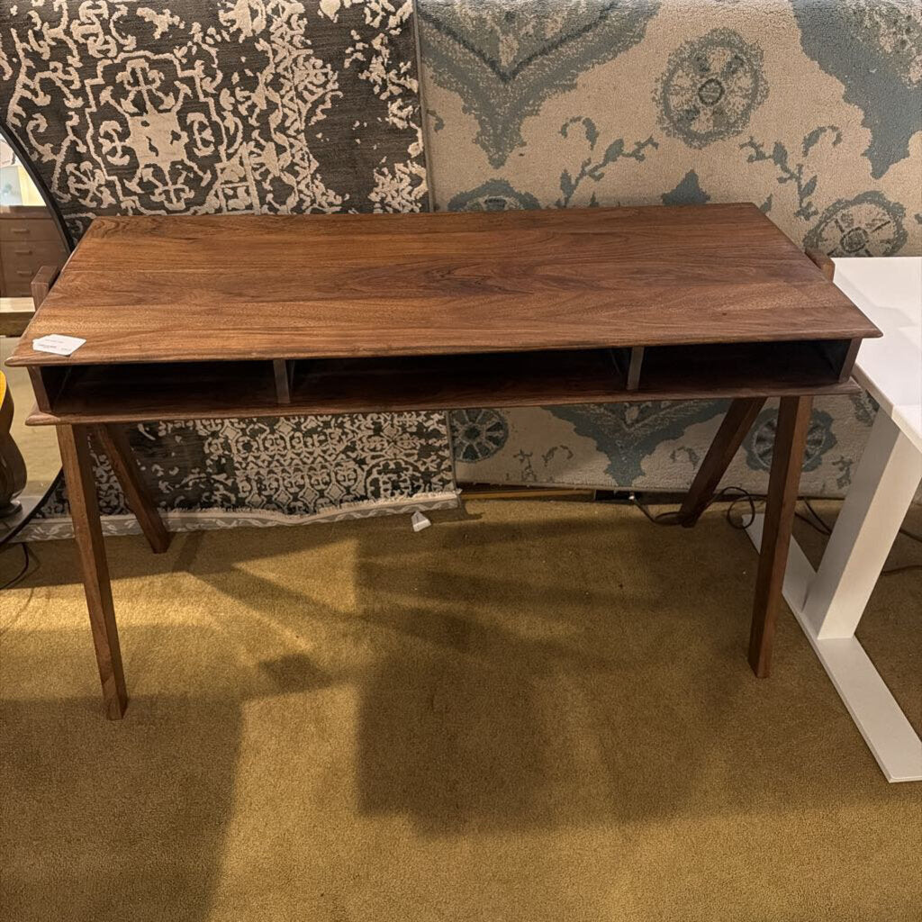 A slim, dark wood writing desk with a minimalist rectangular top, two open storage cubbies, and angled A-frame legs, shown on a neutral carpet.