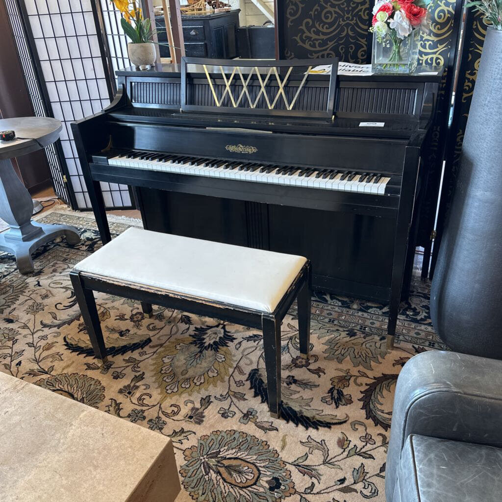Black upright piano with a bench in a room with patterned rug and decorative elements.