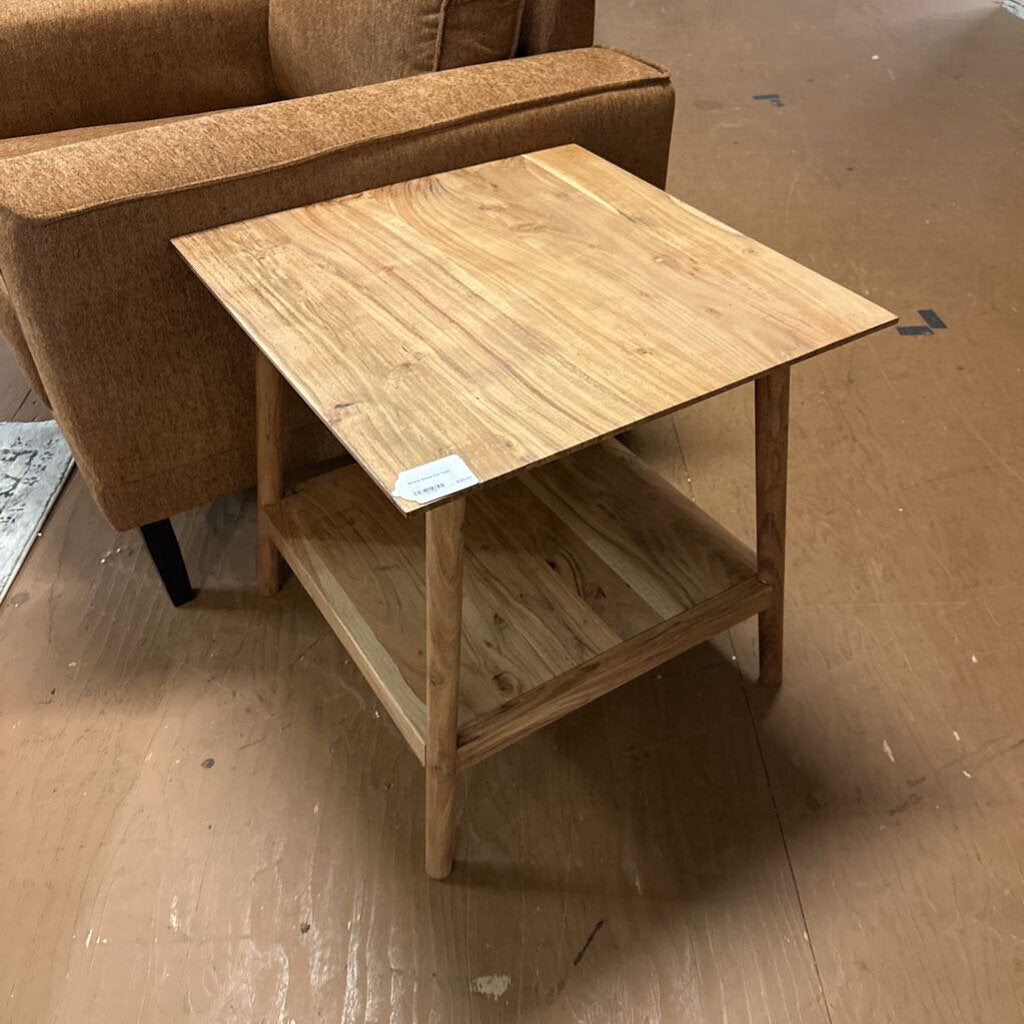 Wooden side table with a brown sofa in the background on a wooden floor.