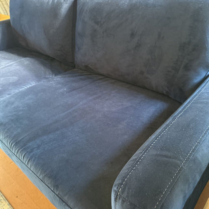 Blue sofa with visible wear and tear on a wooden floor.