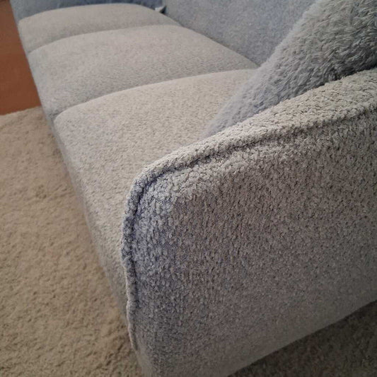Close-up of a textured gray sofa corner on a carpeted floor.