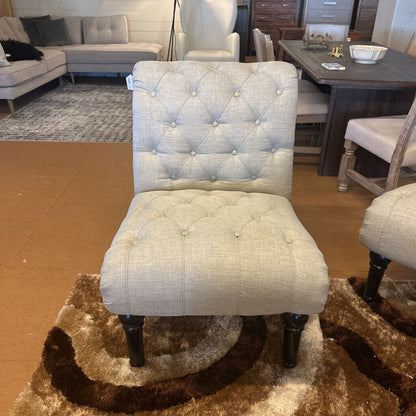 Light gray tufted chair in a furniture store setting with other chairs and a table.