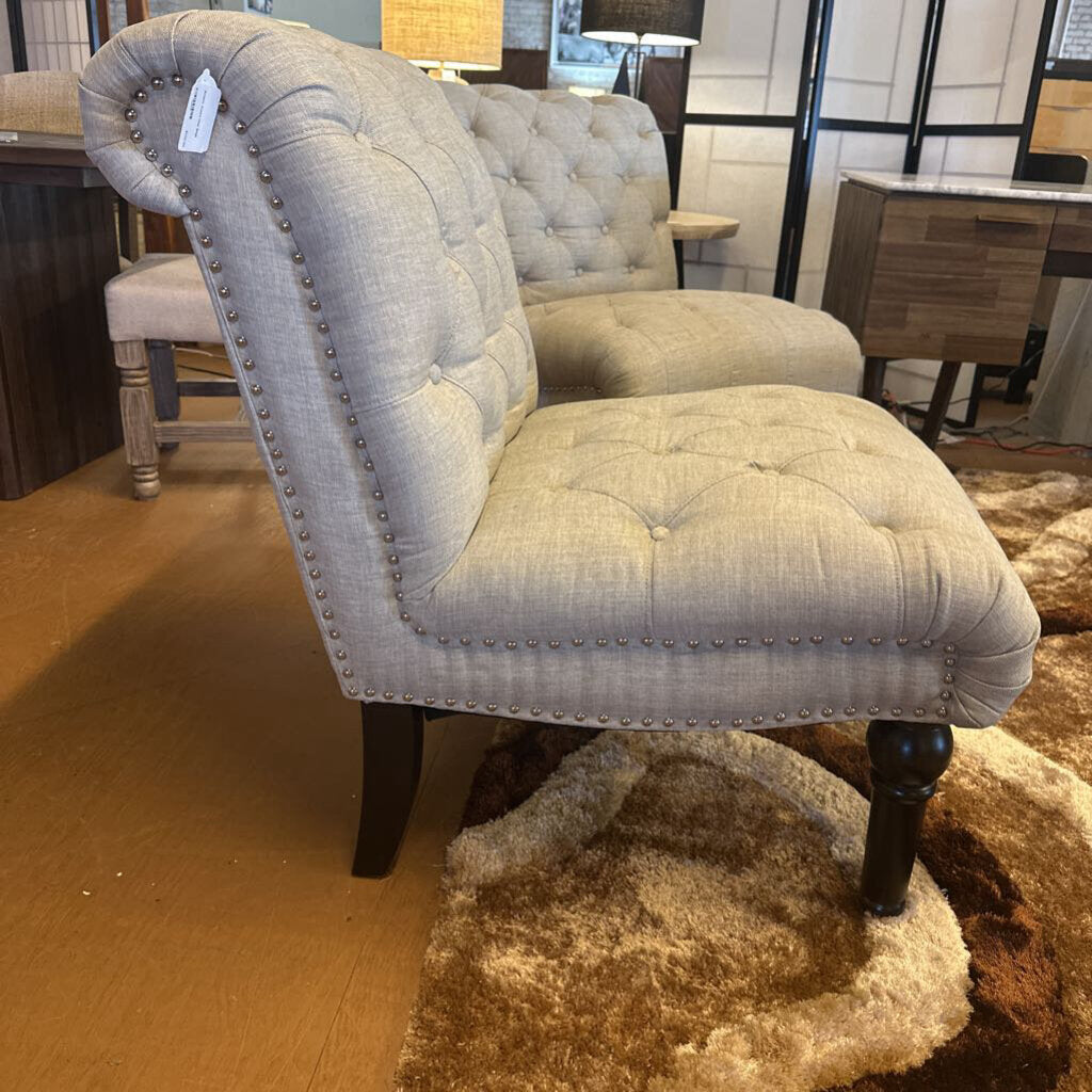 Gray upholstered chair with nailhead trim on a wooden floor.