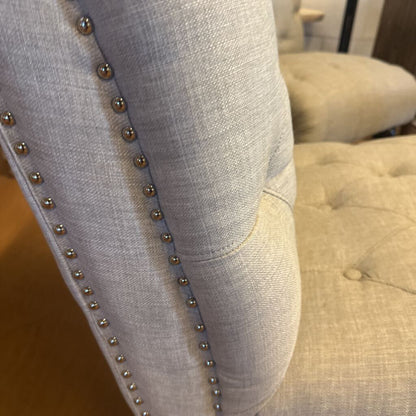 Close-up of a gray upholstered chair with button tufting and metal studs.