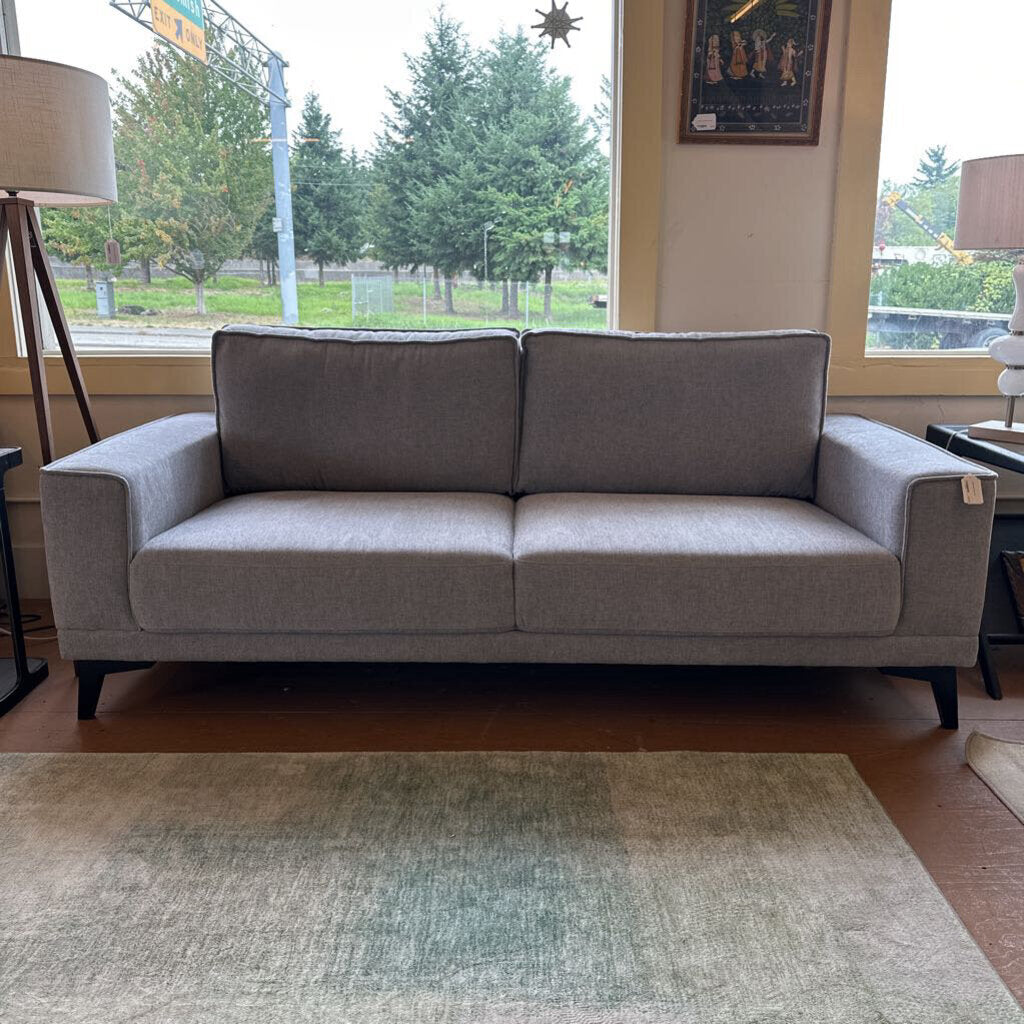 Gray sofa in a room with large windows and a rug on the floor.