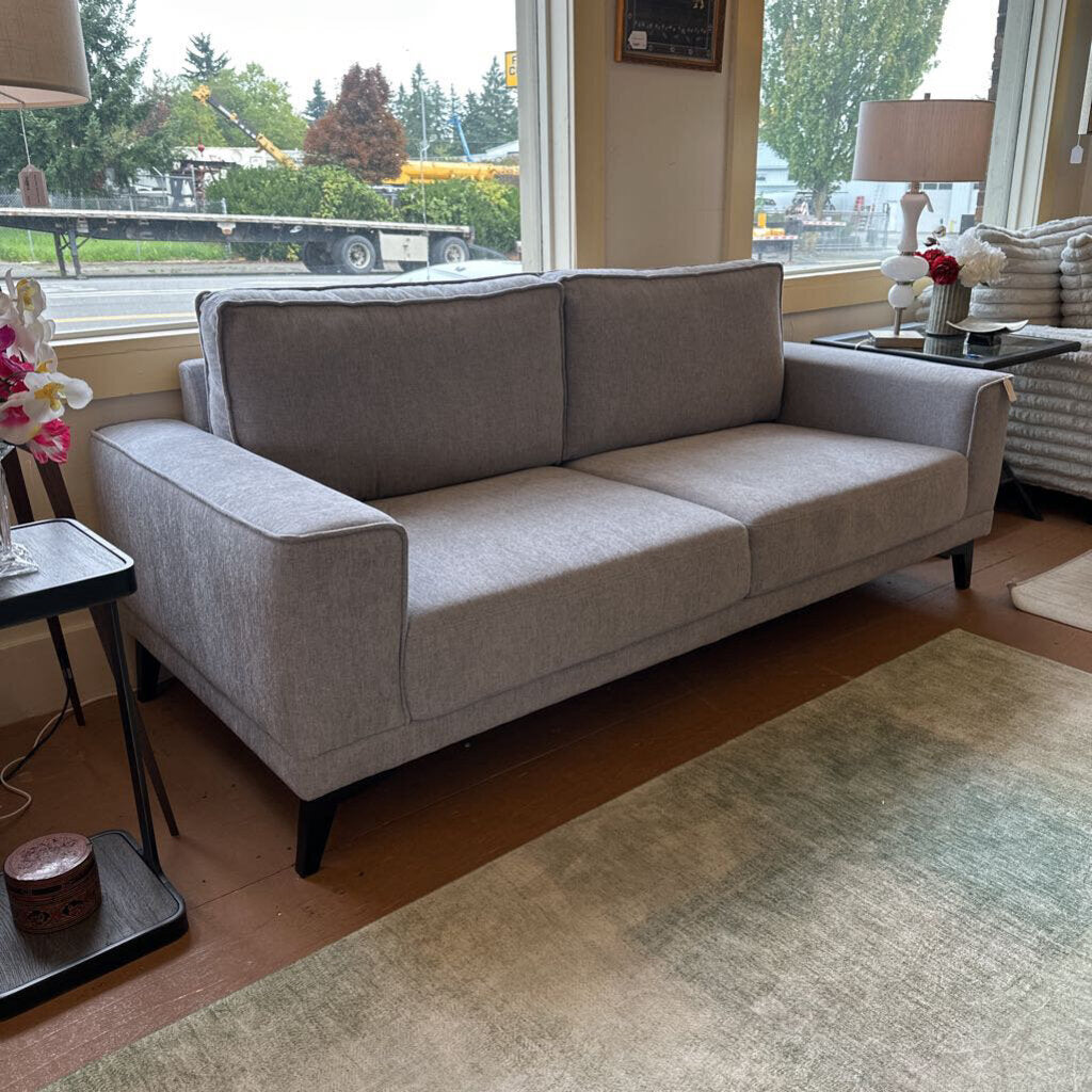 Gray sofa in a room with large windows showing an outdoor view.
