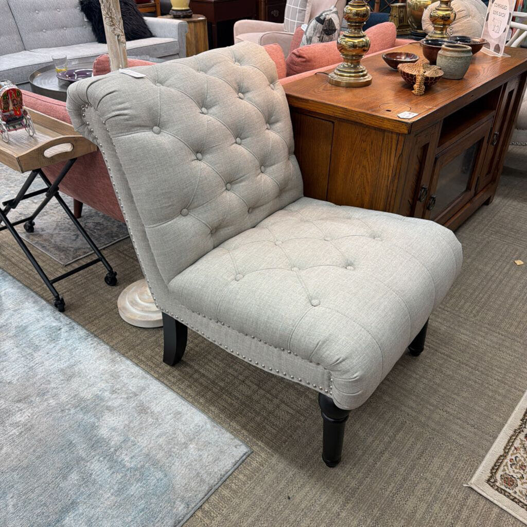 Gray tufted chair in a room with furniture and decor items.