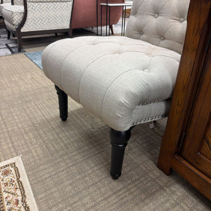 Light gray upholstered chair with tufted backrest and black legs on a carpeted floor.