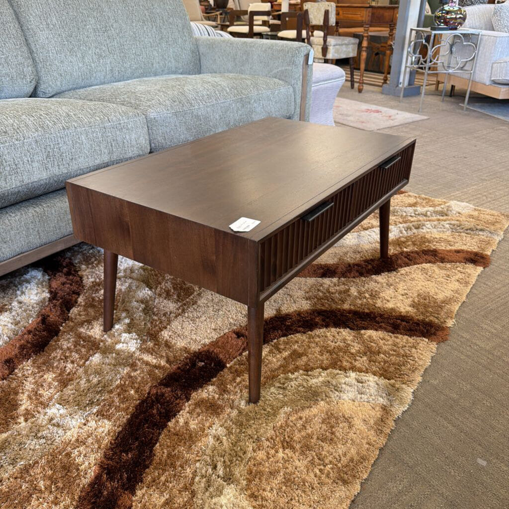 Wooden coffee table on a patterned rug with a gray sofa in the background