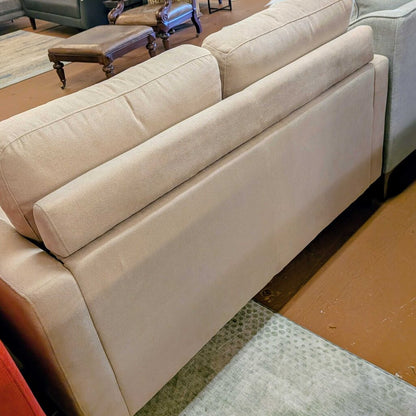 Beige sectional sofa in a room with wooden flooring and furniture.