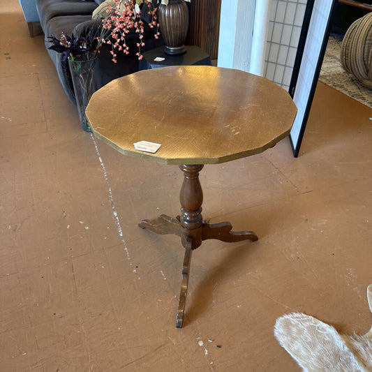 Wooden round table with a pedestal base on a brown floor.