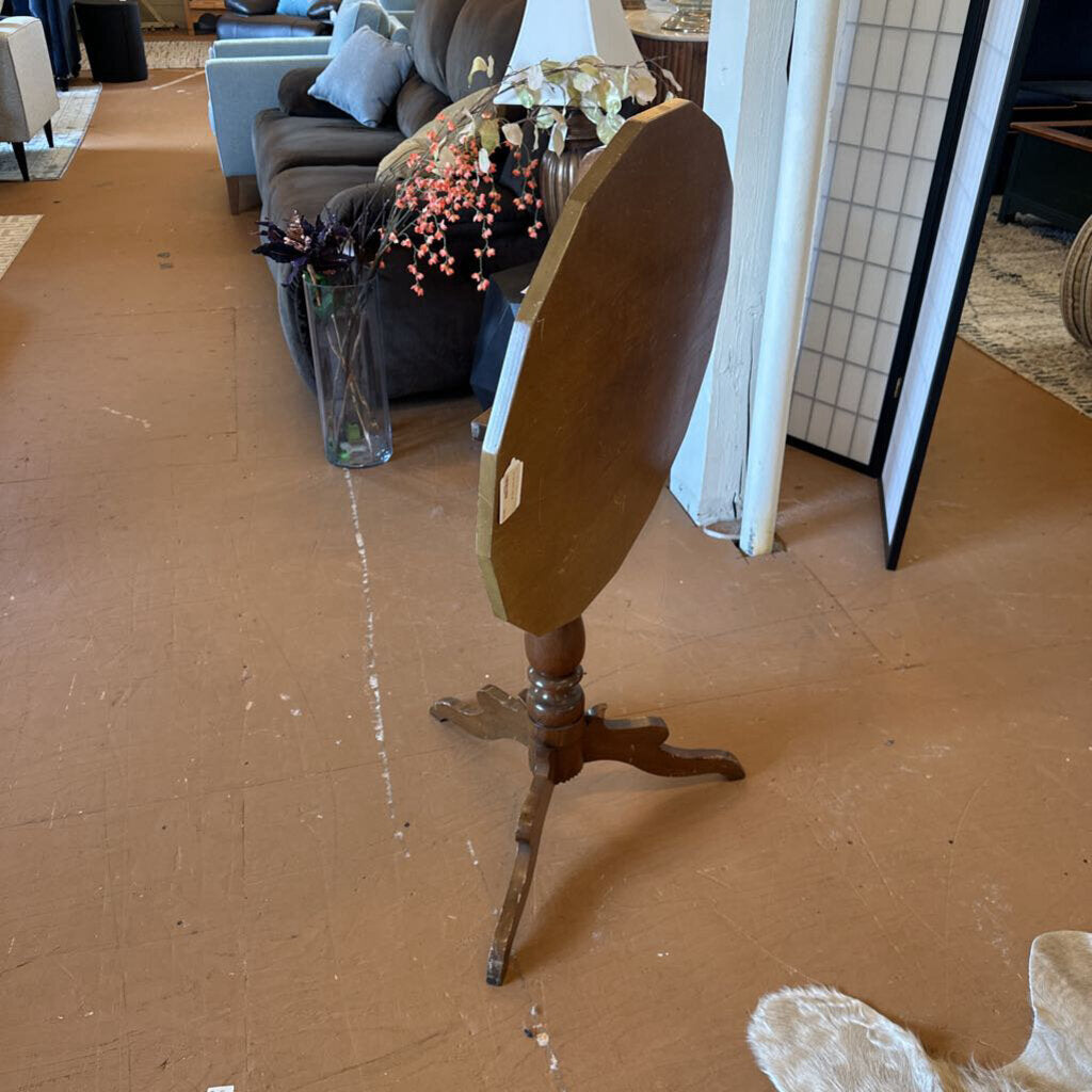 Wooden table with a round top and tripod base in a room with furniture and decor.