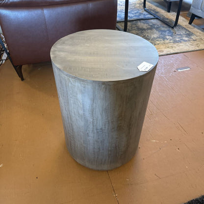 Round wooden side table on a brown floor with a blurred background