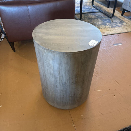 Round wooden side table on a brown floor with a blurred background