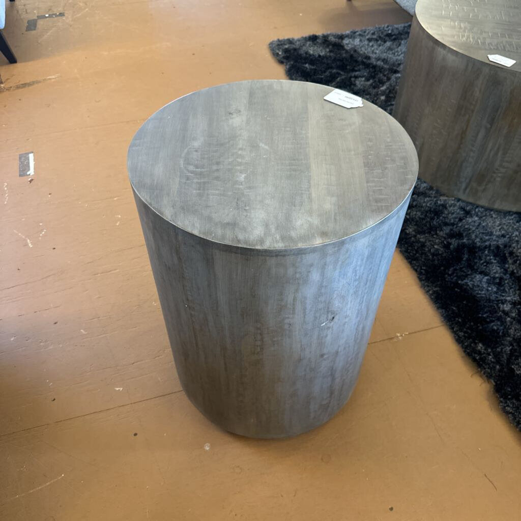 Round wooden stool on a cardboard surface with a black textured rug underneath