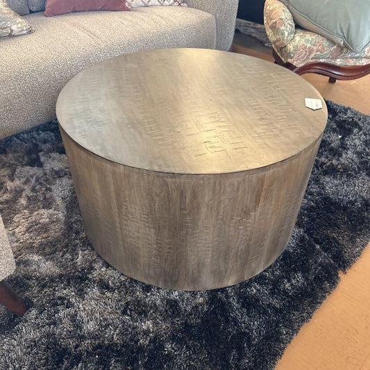 Round wooden coffee table on a dark rug with a blurred background