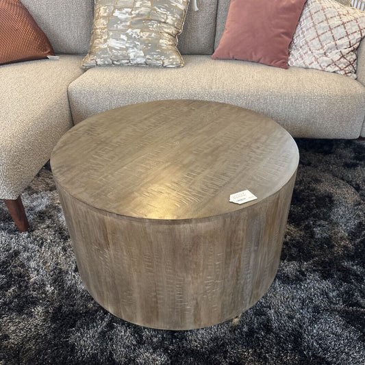 Round wooden coffee table in front of a gray sofa with patterned cushions on a dark rug.