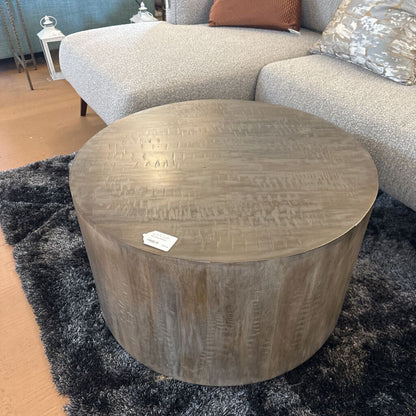 Round wooden coffee table in a living room setting with a sofa and rug.